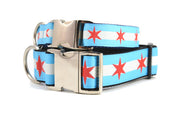 Stack of two dog collars with metal clasps - dog collars have two light blue stripes and one white stripe and red six pointed stars - representing the Chicago Flag.