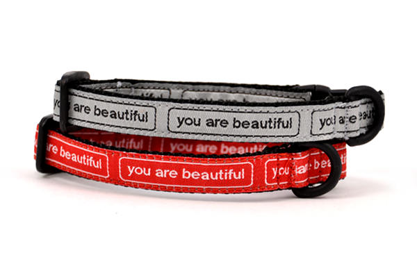 Two cat collars stacked.  One is silver with the words you are beautiful in black.  One is red with the words you are beautiful in white.