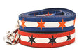 Two Large dog collars stacked.  One has two outer red stripes and one central off-white stripe and black six point stars around the collar. One has two outer dark blue stripes and one central off-white stripe and orange six point stars around the collar. 