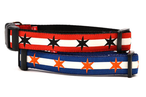 Two dog collars stacked.  One dog collar has two outer red stripes and one central off-white stripe and black six point stars around the collar.  The other collar has two dark blue outer stripes and one inner off white stripe and orange six point stars around the collar.