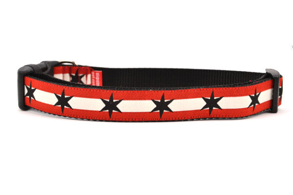 Large dog collar has two outer red stripes and one central off-white stripe and black six point stars around the collar. 