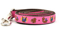 One small pink dog leash - design includes squirrel in lucha libre mask with a yellow flower behind it and a tulip on the mask.  One small squirrel with a tulip in its mouth and one with a tulip bulb.  Also, a six pointed star.