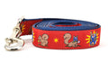 One large red dog leash - design includes squirrel in lucha libre mask with a yellow flower behind it and a tulip on the mask.  One small squirrel with a tulip in its mouth and one with a tulip bulb.  Also, a six pointed star.