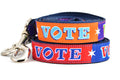 Two dog leashes stacked.  One is purple and orange blocks pattern with the word VOTE on each color block. One is red and navy blocks pattern with the word VOTE on each color block.  