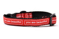 Cat collar that is red with the words you are beautiful in white.